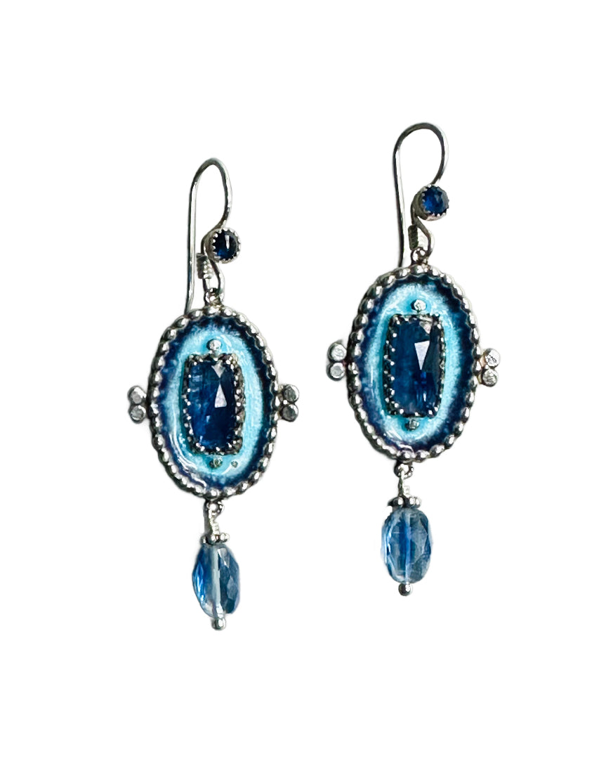 The earrings have a gorgeous rectangular rose cut blue kyanite framed in a delicate lacy bezel in the center of the piece. The main stone is surrounded by enamel that is interrupted by a wall of small silver dots that go all around the edge of the oval shaped piece. From the piece hangs a faceted oval kyanite &nbsp;stone and a 3mm rose cut blue sapphire accent is on the ear wire.