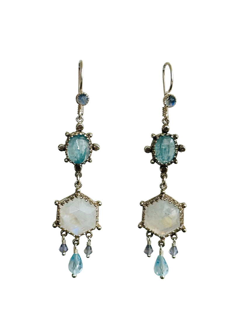 These elegant earrings are a versatile medium &nbsp;size chandelier. They feature a rose cut hexagon rainbow moonstone framed in a delicate lacy bezel with an open back to let the light shine through.

From the hexagon hangs a faceted blue topaz drop with two small faceted iolite drops on either side.&nbsp;

Above the hexagon is an oval rose cut aqua kyanite set in a bezel with silver dot adornments. The ear wires have a rainbow moonstone accent.

Materials: Recycled Sterling Silver, rainbow moonstone, Blue