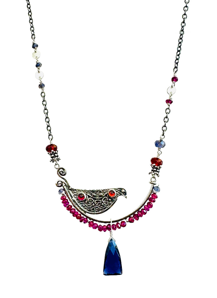 Garnet & Iolite Beaded Bird Necklace - Silver

This is a whimsical, fun, and unique necklace!

The bird sits on a silver arch that has a beautiful floral pattern. The bird is engraved and has a detail wing on both sides. On the front side of the bird, there are two gems set.

The silver arch has a border of 3mm faceted rhodolite garnet with an iolite accent at either end, a rose cut rhodolite garnet and hessonite garnet gems are set in a silver bezel near the tail and head, and a beautiful fancy cut iolite