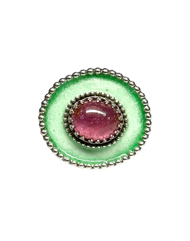 A horizontal 1"x7/8" oval with a light green with a darker green border enamel,  has a 11x9mm beautiful cabochon pink tourmaline set in the center, in a lacy bezel. The band has a delicate floral pattern, is 1/8" and sturdy.    This ring is a size 8.5  Materials: Sterling silver, enamel & pink tourmaline  This ring is unique, fun, beautiful and colorful!    