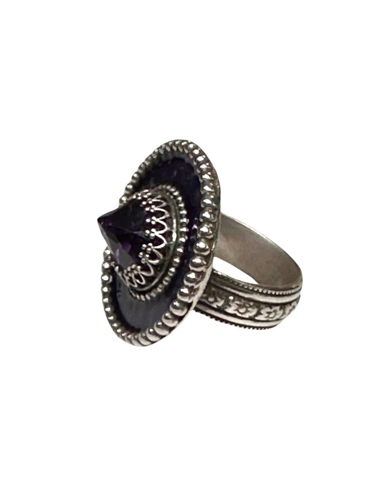  A horizontal 1"x7/8" oval with purple enamel and an 11x9mm Amethyst set in the center, in a lacy bezel. The band has a delicate floral pattern, is 1/8" and sturdy. This ring is a size 6.5