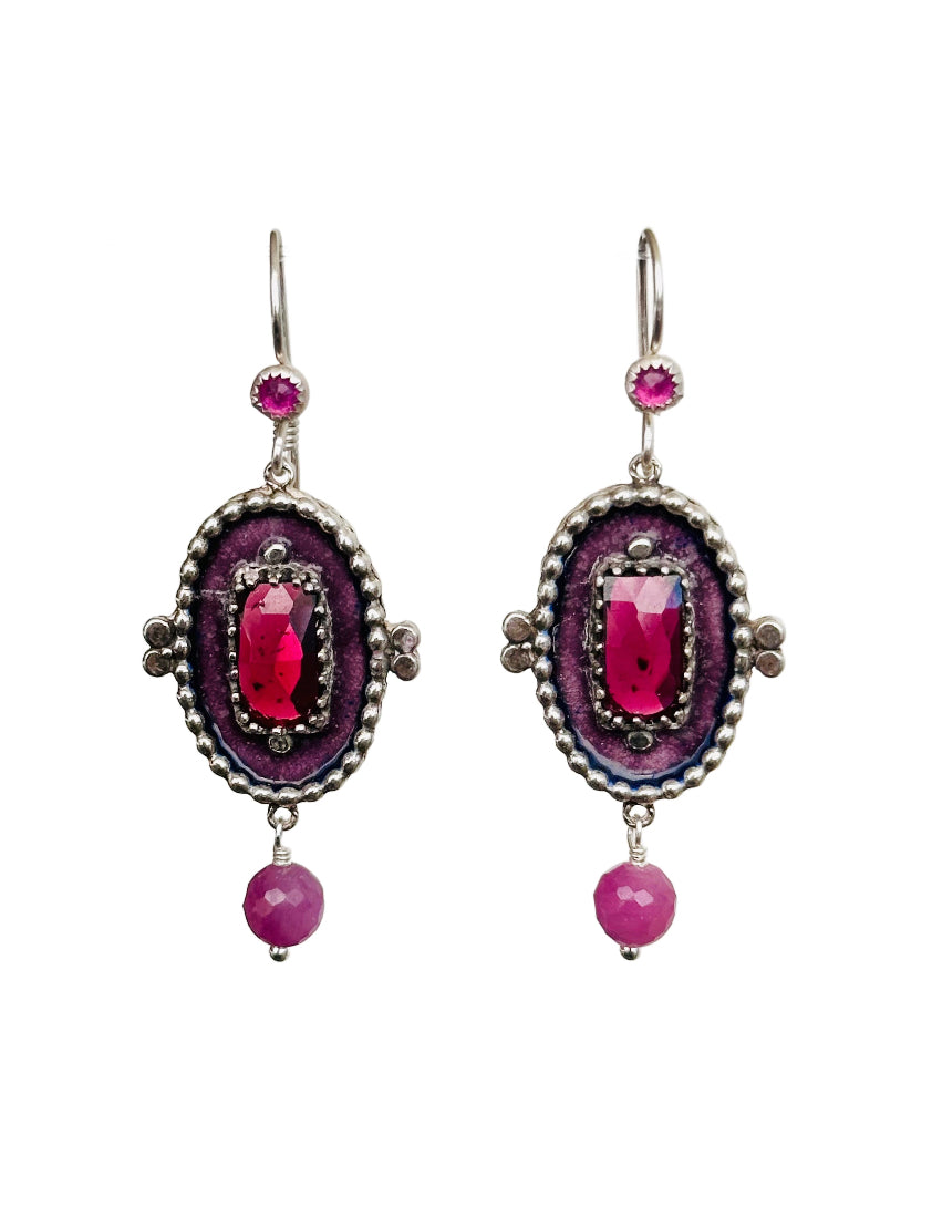 These colorful earrings are a beautiful mix of metalsmithing, enamel and gems! They are a medium sized statement earring which will add a pop of color to your outfit and day!&nbsp;

The earrings have a gorgeous rectangular rose cut rhodolite garnet framed in a delicate lacy bezel in the center of the piece. The main stone is surrounded by enamel that is interrupted by a wall of small silver dots that go all around the edge of the oval shaped piece. From the piece hangs a faceted pink sapphire stone and a 3m